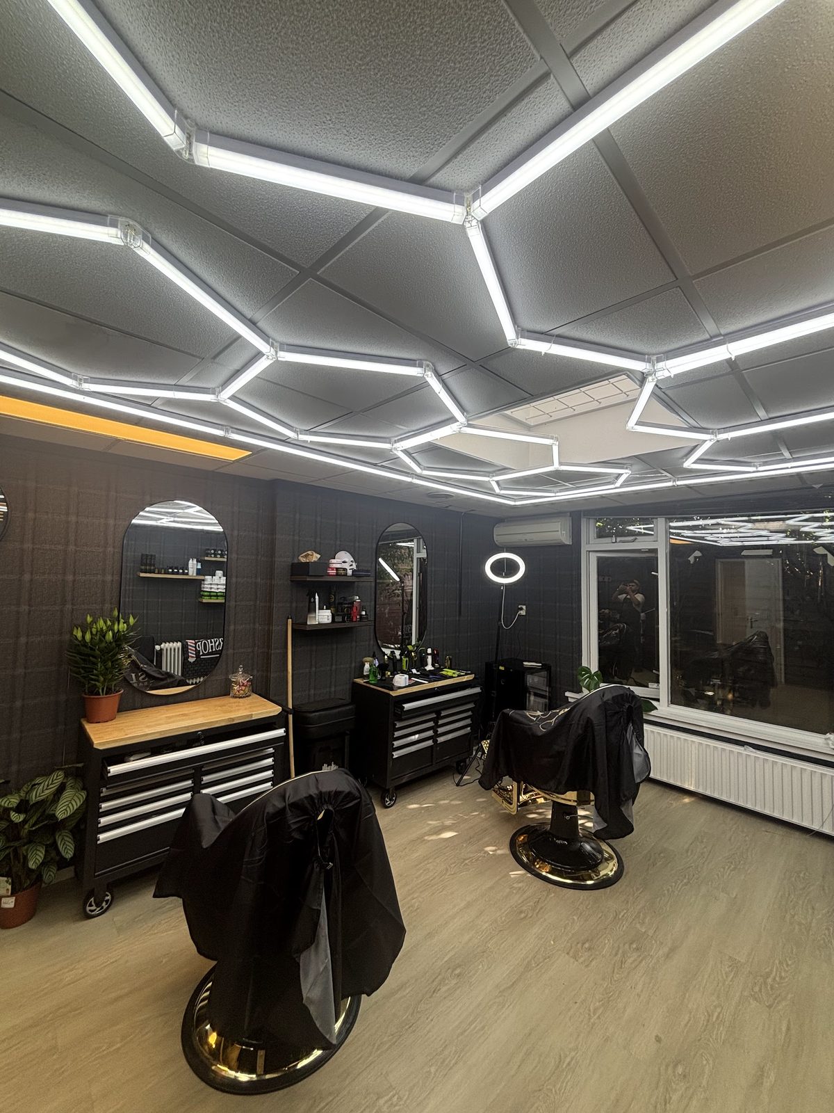 De zaak van Slow Barbershop met het zeshoekige ledplafond, een kappersstoel, de gereedschapskar en de ringlamp