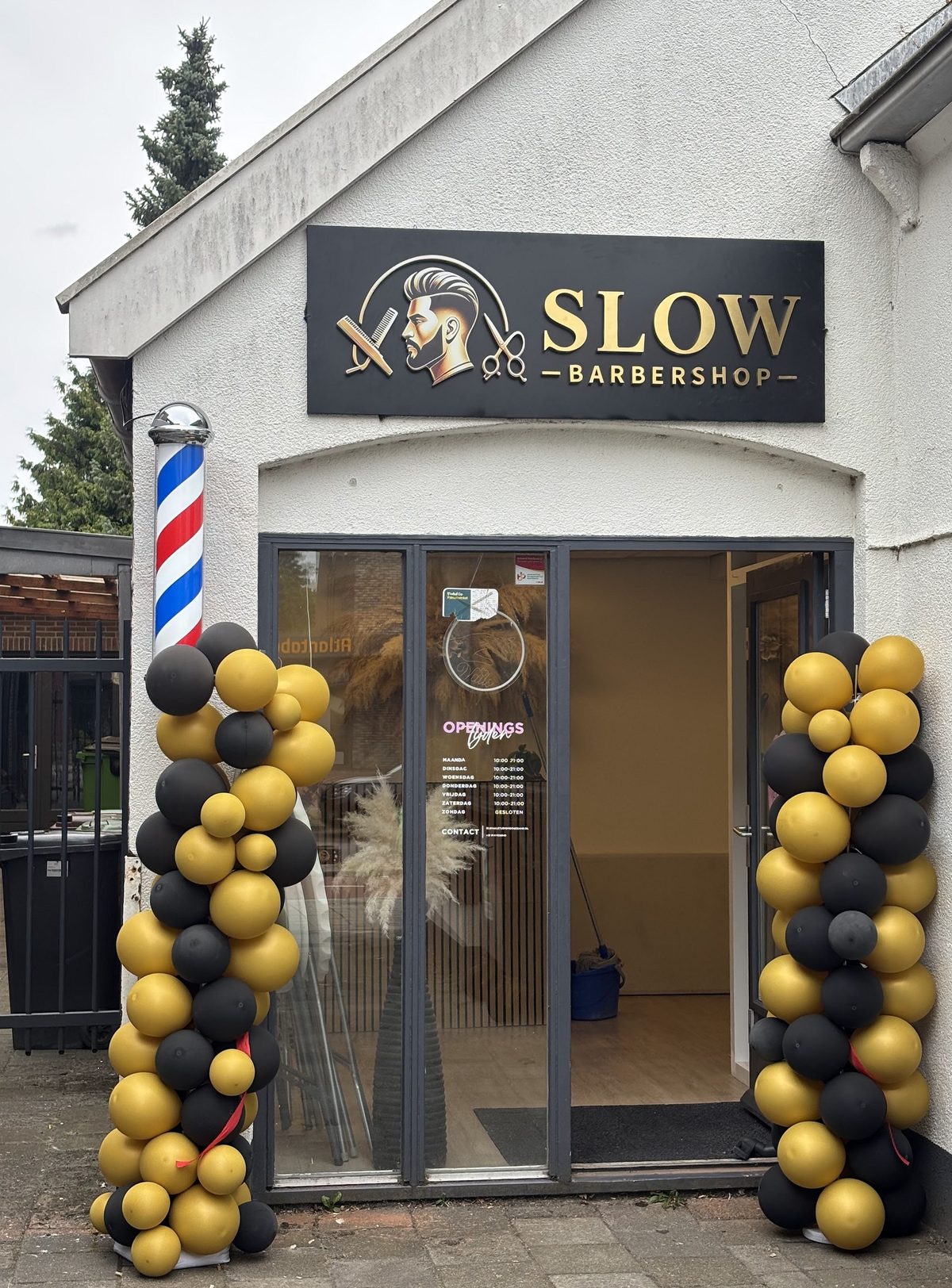 De voorkant van Slow Barbershop aan de Kerkstraat, met het zwart-gouden bord, de barberpaal en zwart-gouden ballonnen bij de deur